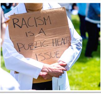 Person Carrying Racism is a Public Health Issue Sign